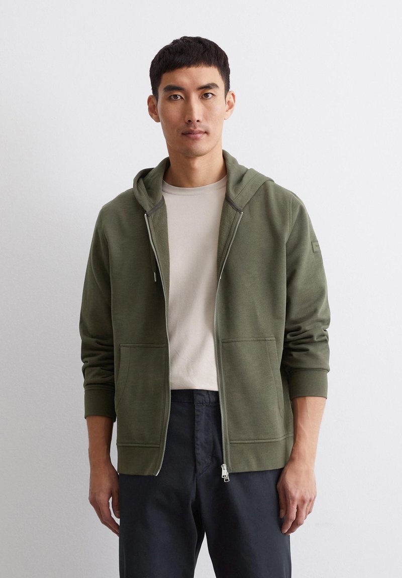 Olivgrüner Zip-Hoodie aus weichem Baumwoll-Mix, mit einem Front-Reißverschluss, zwei Taschen, gerippten Säumen und einer gemütlichen, verstellbaren Kapuze.
