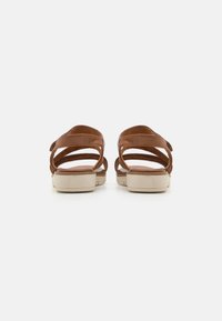 Sandali in pelle marrone con cinturini incrociati e suola chiara, dotati di tacco basso e texture liscia.
