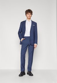 Marineblauer Anzug mit passender Hose, darunter ein weißes Hemd, glattes Material, taillierte Passform, einreihiger Blazer, minimalistisch im Design.