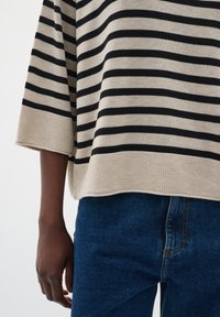 Maglione oversize a righe beige e nero con orlo a costine e maniche larghe, abbinato a jeans blu scuro con una superficie liscia.