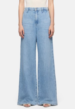 Lyseblå, højtaljede, vide jeans med ombuk, båret med åbne sandaler med åben tå; beskåret fra midt på torso til gulvlængde, hænder afslappet ved siderne.