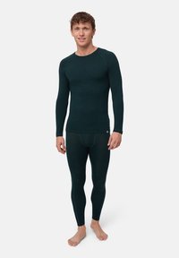 Mörkgrön långärmad termotröja och matchande leggings gjorda av strukturerad väv. Ajusterad passform med rundad halsringning och minimal varumärkning.