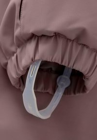 Ljuslila tyg med en texturerad yta. Har en samlad elastisk ärmslut och en genomskinlig plastspänne för justering.