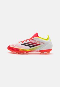 White football cleat with vibrant red, yellow, and black accents. Features a textured mesh upper and a molded sole with transparent studs.