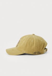 Khaki cotton baseball cap with a curved brim, embroidered logo on the front, and adjustable strap at the back. Textured fabric finish.