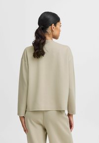 Beige sweatshirt med en afslappet pasform, rund halsudskæring og nedsatte skuldre, lavet af blødt materiale. Vist fra ryggen, med matchende bukser.