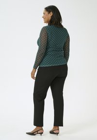 Langärmliges türkisfarbenes Top mit weißen Punkten, durchsichtigen Mesh-Ärmeln, kombiniert mit schwarzen Slim-Fit-Hosen und schwarzen Slingback-Absätzen.