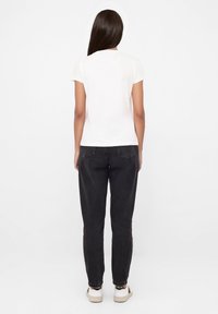 Korte mouwen, witte top gecombineerd met loszittende, zwarte jeans. Opvallende details zijn het eenvoudige ontwerp en minimalistische hardwareaccenten.
