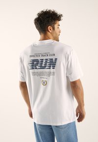 White cotton t-shirt featuring a graphic print on the back with "RUN" in blue, text detailing, and a logo at the bottom. Standard fit.