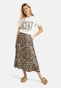 Beiger T-Shirt mit Leopardenmuster-Text "Duft des Sommers", kombiniert mit einem fließenden, leopardgemusterten Maxirock und hellbraunen Slidesandalen.