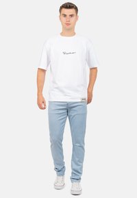Witte T-shirt met een zwart logo, gecombineerd met lichtblauwe gestreepte broek en witte sneakers. Eenvoudig ontwerp met korte mouwen en eenRelaxte pasvorm.