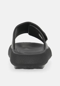 Black slip-on sandal with a textured footbed, open back, and a simple strap. Made from flexible material with a modern, minimalist design.