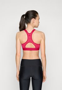 Sujeción deportiva en rojo brillante con un diseño de espalda deportiva y corte abierto. Combinada con leggings negros de talle alto, que presentan una textura suave.