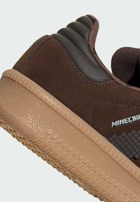Braune Sneaker mit einem strukturierten, braunen Wildleder-Obermaterial, dunklen Lederelementen und einer gummiartigen Sohle in Beige mit geometrischem Muster. Mit "Minecraft"-Markierung.