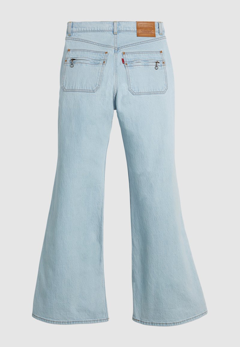 Jean évasé bleu clair en denim, avec une taille haute, deux poches arrière avec des détails de couture, et une étiquette en cuir à la ceinture.