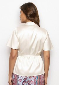 Korte mouwen, crèmekleurig satijnen top met een kraag en elastische tailleband, gladde textuur en een lichte glans, gecombineerd met een patroonbroek.