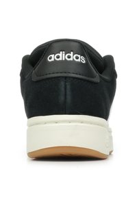 Czarne zamszowe trampki z białą gumową podeszwą, z czarną skórzaną nasadką na pięcie oznaczoną białym napisem "adidas". Widoczny wypukły detal szwów.
