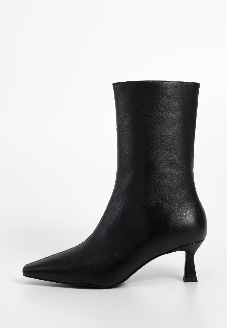 Stivale alla caviglia in pelle nera con punta affilata, design elegante e tacco kitten modesto. Texture liscia con minimalismo negli accessori in metallo.
