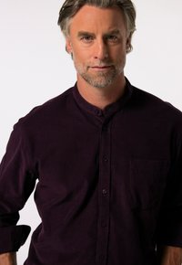 Camicia da uomo in un elegante viola scuro con colletto alla cinese, dotata di una tasca sul petto e una texture morbida. Design semplice e informale.