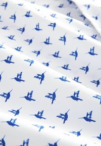 Tessuto bianco con un motivo ripetuto di piccoli uccelli blu in volo. La trama è liscia e leggera.