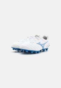 Des chaussures de football blanches avec des accents bleus, présentant une tige texturée, un système de laçage, et six crampons proéminents sur la semelle extérieure pour une meilleure traction.
