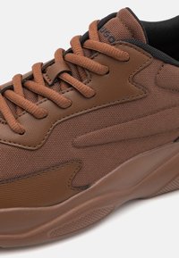 Kengät, joissa on ruskea kangas, tekstuuripinta, kengännauhakiristys ja pehmustettu nilkkaosa. Varustettu vahvalla kumipohjalla, jossa on kuvioitu kulutuspinta.