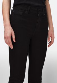 Černé džíny z denimu s úzkým střihem, zapínáním na zip a klasickým pětiokolkovým designem. Hladká textura s jemnými švy na kapsách.