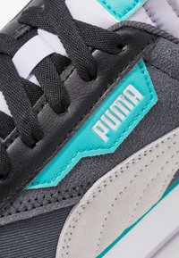 Sneaker nero e grigio con materiali in suede e leather. Presenta accenti turchesi, lacci neri e un logo bianco. Superficie testurizzata.