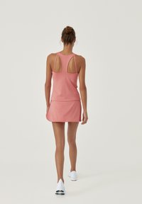 Rosa sportklänning med en åtsittande överdel som har öppningar i ryggen och en utsvängd kjol. Tillverkad av elastiskt material, designad för aktiv användning.