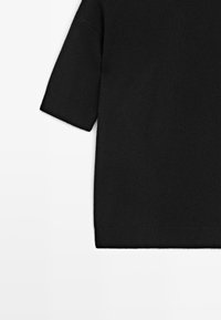 T-shirt nero a maniche corte in maglia con una texture liscia, vestibilità comoda e polsini a costine. Le spalle senza cuciture migliorano comfort e stile.
