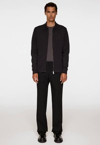 Svart jacka med dragkedja och krage, kombinerad med en grå t-shirt och svarta byxor. Slät textur, minimalistisk design och inga synliga mönster.