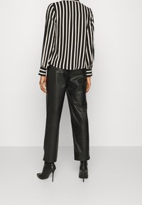 Blusa a righe bianco e nero con maniche lunghe, abbinata a pantaloni in pelle nera a vita alta e stivali neri alla caviglia.