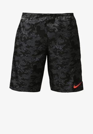 Mann läuft und trägt ein helloranges Nike-Sportshirt, schwarze Camouflage-Shorts, weiße gestreifte Socken und schwarze Sportschuhe.