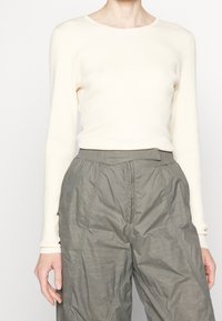 Maglietta a maniche lunghe color crema a coste con collo rotondo, abbinata a pantaloni grigi larghi e strutturati con vita elasticizzata e dettagli di cucitura.