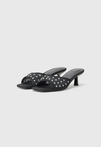 Sorte åpen-tå sandaler med en teksturert overdel som har sølvnagler og en kort, solid hæl. Designet inkluderer kryssede stropper for støtte.