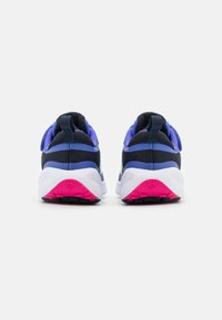 Zapatillas deportivas azules y moradas con una suela blanca y detalles en rosa; cuentan con un upper texturizado y un tirador en el talón.