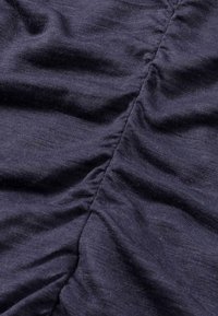 Dunkelblauer Stoff mit subtiler Textur, der entlang der Naht geraffte Details aufweist und sanfte, fließende Linien erzeugt.