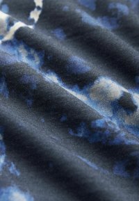 Textureret stof i nuancer af blå og sort, med et subtilt sky-lignende mønster. Blød, glat overflade med bølgede folder.