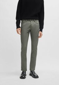 Groene textuurbroek met een slim fit, gemaakt van een geweven stof. Voorzien van een knopsluiting aan de voorkant en achterzakken. Gecombineerd met zwarte schoenen en een zwarte trui.