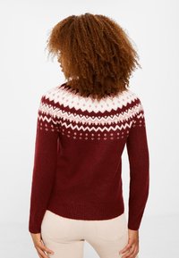 Vínový pletený svetr s bílým geometrickým vzorem na průramcích a dlouhými rukávy, s žebrovaným lemem a měkkou texturou.