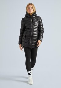 Juodas pūkinis džemperis su gobtuvu, užtrauktuku priekyje ir tekstūruotu paviršiumi. Turi šonines kišenes ir reguliuojamą pritaikymą. Derinamas su juodomis tamprėmis.