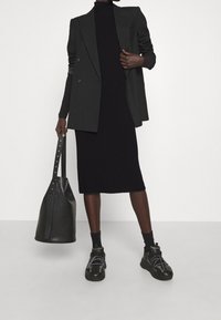 Abito nero a coste con collo alto, abbinato a un blazer oversize nero. Accessoriato con una grande borsa nera e sneakers nere chunky.