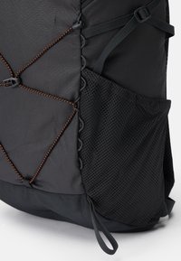 Mochila negra con tejido texturizado, detalles de cordón elástico con acentos en naranja y un bolsillo lateral de malla para almacenamiento adicional.