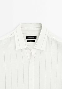 Chemise en lin blanc avec de fines rayures noires verticales, col classique et étiquette de marque noire "Massimo Dutti" à l’intérieur de l'encolure.