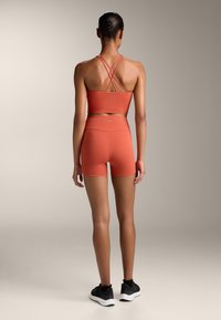 Korall színű sportos felső és magas derekú short kombinációja. Simább, rugalmas anyagból készült, minimális márkajelzéssel.