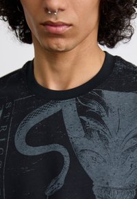 Sort t-shirt med et gråt grafisk design af en slange, der er sammenflettet med blomstermotiver. Rund hals med et struktureret stof.