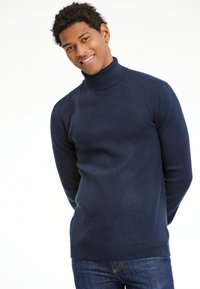 Navyfarbener Rollkragenpullover aus glattem Stoff, mit langen Ärmeln und einer taillierten Passform, kombiniert mit blauen Jeans.