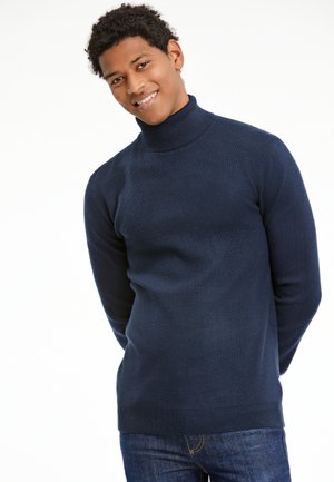 Navyfarbener Rollkragenpullover aus glattem Stoff, mit langen Ärmeln und einer taillierten Passform, kombiniert mit blauen Jeans.
