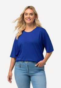 Blue oversized t-shirt with short sleeves, round neckline, smooth texture, paired with light blue jeans, featuring pockets and slight distressing.