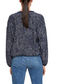Marineblaues Sweatshirt mit langen Ärmeln, verziert mit floralen Designs und elastischen Bündchen. Kombiniert mit hellblauen Jeans, die Taschen zeigen.